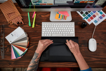 Professional web designer. Top view of male hands using digital graphics tablet and desktop in the office or studio. Workplace with graphic tablet, keyboard, computer and color swatches