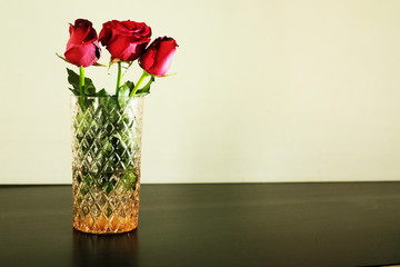 Three red roses in glass vase on white background