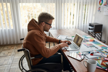 Creative professional. Side view of young male UX UI designer in a wheelchair designing new mobile...