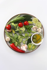 Raw green vegetables on the round white plate. Flat lay Tomatoes, broccoli, cucumber, garlic, broccoli. olive oil, lime, mushroom