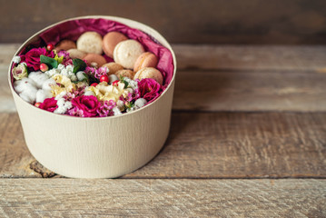 Gift or present with flower and french macaroons on grunge wooden background with copy space. Rustic style. Toned image.