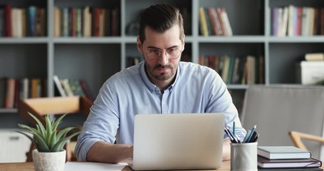Focused business man entrepreneur typing on laptop doing research. Young male professional using computer sitting at home office desk. Busy worker freelancer working on modern tech notebook device. - Powered by Adobe