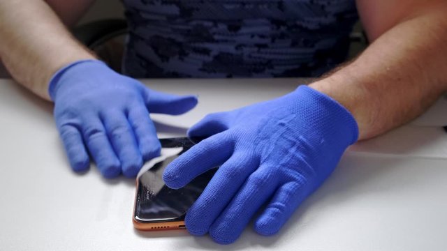 male hand in blue gloves replaces a broken tempered glass screen protector for a smartphone. A man prepares a smartphone to replace glass. Smartphone repair concept