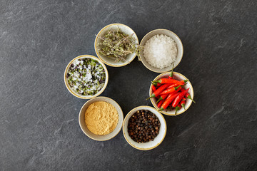 food, culinary and eating concept - bowls with different spices on slate stone table