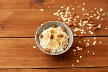 food and breakfast concept - oatmeal porridge in bowl with sliced banana, almond nuts and cinnamon on wooden table