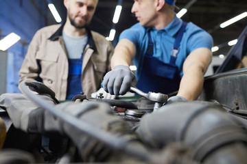 Professional auto mechanic chatting with his colleague while fixing car engine detail, horizontal...