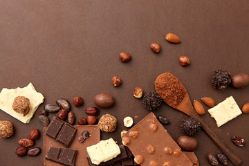 confectionery and food concept - milk, dark and white chocolate bars with nuts, candies, cocoa beans and powder on brown background