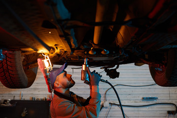 Professional auto mechanic standing under car fixing its parts, horizontal shot, copy space