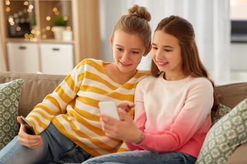 people, technology and friendship concept - happy teenage girls with smartphones sitting on sofa at home