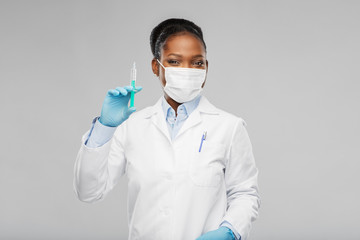 medicine, vaccination and healthcare concept - african american female doctor or scientist in mask with syringe over grey background