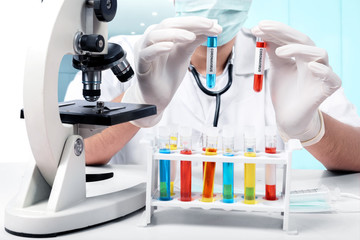Fototapeta premium Doctor man in protective gloves with microscope holding test tubes with a coronavirus blood sample
