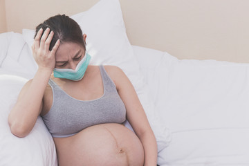 Asian Pregnant woman lays on her bed after wearing protection face mask or hygiene protective mask...