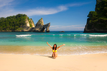 Fototapeta na wymiar young happy and attractive Asian Japanese woman in bikini excited at paradise beach sitting on sand by the sea enjoying idyllic Summer holidays at beautiful tropical