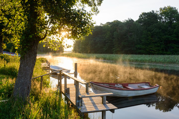 Rowboats moored on a sunlit and misty lake. Sweden © Mikael