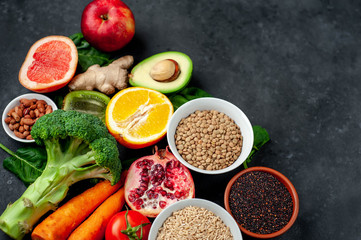 Selection of healthy food:  fruits, seeds, cereals, superfoods, vegetables, leafy vegetables on a stone background. Healthy food for humans. Copy space for your text.