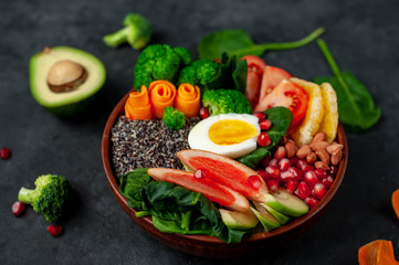 Bowl of Buddha,quinoa, orange, avocado, grapefruit, tomato, pomegranate, spinach, carrots, broccoli, egg in a bowl on a stone background.