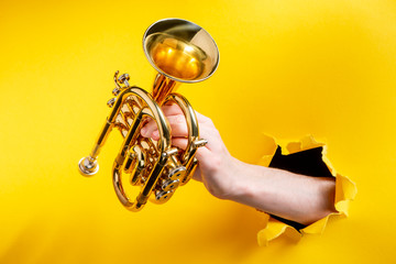 Hand holding a golden trumpet through torn yellow paper background