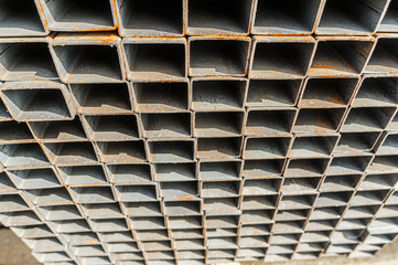 Background close up metal square pipes in stock. Stacks of new square steel pipes at the factory