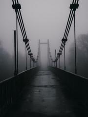 The old bridge over the river in the early foggy dark cold morning. Mysterious scary landscape
