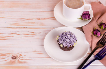 Chocolate delicious cupcake with cream and fragrant coffee with milk on a white wooden table.