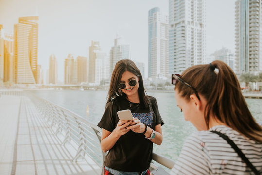 Two Attractive Girls Are Standing In Dubai Marina And Using A Mobile Phone