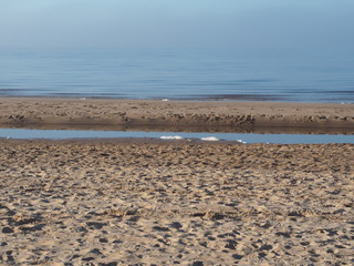 Footprints in the sand of the seashore. Light fog. Blue sky.