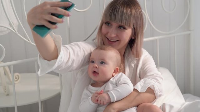 mom with baby in bed taking selfies on smartphone