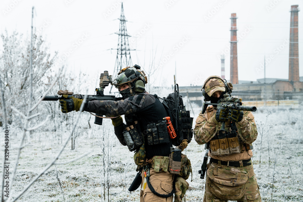 Wall mural men in camouflage cloth and black uniform with machineguns side to side with factory on background. 