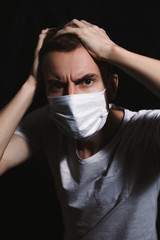 Frightened young guy in a medical mask. Young man in a protective mask against viruses panicky clutching his head