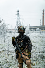 Man in black camouflage uniform hold machinegun. Soldier in the winter with factory on background....