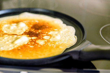 pancake frying pan with crepe pancake cooking on cooker in kitchen