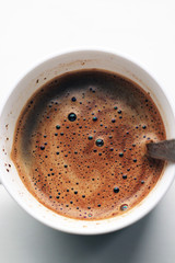 black coffee with foam in white mug with metal vintage spoon