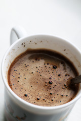 black coffee with foam in white mug with metal vintage spoon