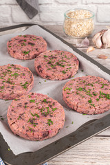 Raw veggie burger with beetroot and white beans with parsley leaves on wood cutting board.