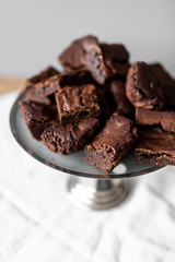 Pieces of chocolate brownie on a silver tart plate on white linen and wooden table