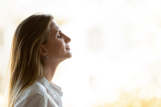 Side view close up head shot young mindful businesswoman breathing fresh air, managing stress at office. Calm peaceful millennial female manager, company owner or team leader meditating at workplace.