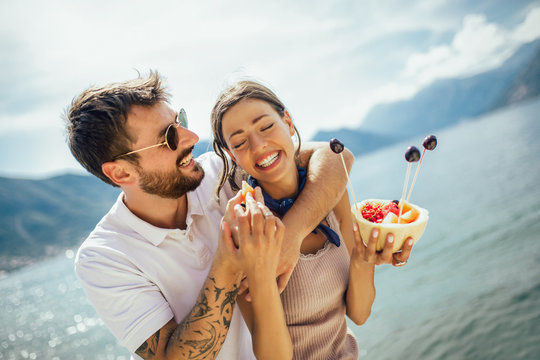 Young Couple Eating Fruit On The Beach- Summer Party With Friends And Healthy Food Concept