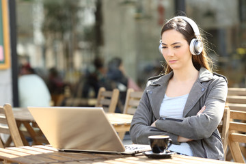 Serious girl watching media on laptop with headphones on a terrace