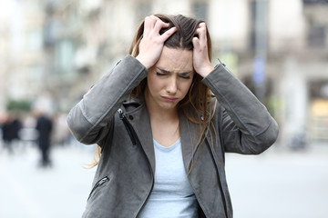 Stressed girl grabbing head complaining on city street