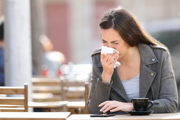Woman blowing her nose with tissue on a coffee shop