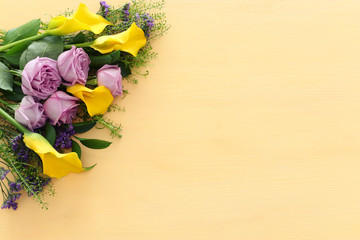 summer bouquet of pink roses and yellow calla lily flowers over wooden pastel background. top view, flat lay