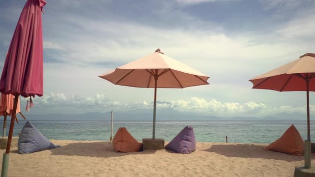 view of beautiful and tranquil beach scene with sea in the horizon and breeze blowing softly on sun umbrella on the sand in Summer holidays travel and tropical tourist destination concept