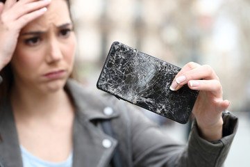 Worried woman holding broken smartphone on street