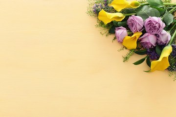 summer bouquet of pink roses and yellow calla lily flowers over wooden pastel background. top view, flat lay