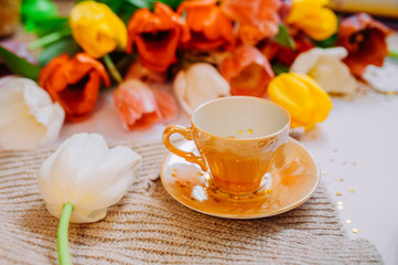 spring tea party. small gold cups with saucer on a light background with a bouquet of colorful tulips.