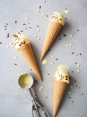 Eistüten mit Vanilleeis, Schokoladestreusel, Herzen und einem Portionierer auf einem grauen Hintergrund, Flat lay, Sommer, Dessert, servierfertig