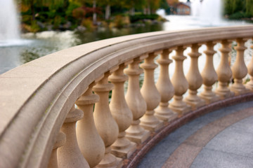 Close up stone railings in front of a pond with fountains. Beige handrail fence.