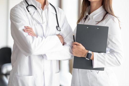 Cropped close up image young medical workers standing together. Male doctor with phonendoscope and folded hands standing near female young nurse with documents in folder, medical insurance concept.