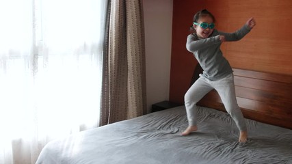 Slow motion of happy little asian girl dancing jumping on the bed with swimming glasses joyful kid playing having fun at home 4k slow motion footage 