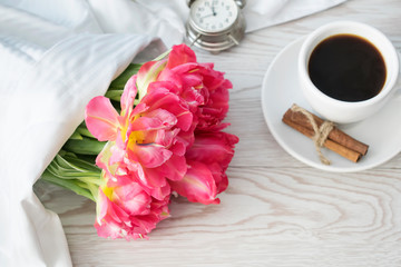 Women's day concept. Greeting card with pink tulips and coffee on white wooden background. Copy space, top view.